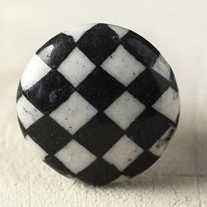 Może przedstawiać: Czarno-biały ceramiczny gałka. Gałka ma lekko wypukłą, fakturowaną powierzchnię.