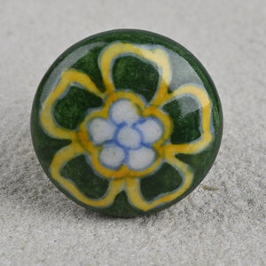 May include: A green ceramic knob with a yellow and white flower design.