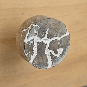 以下が含まれることがあります： ユニークな自然なパターンを持つ、丸いグレーとホワイトのノブ。ノブは木でできており、滑らかで磨かれた仕上げになっています。