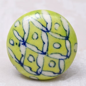 Op de afbeelding: Een ronde keramische knop met een groene achtergrond en een wit en blauw bloemenpatroon.