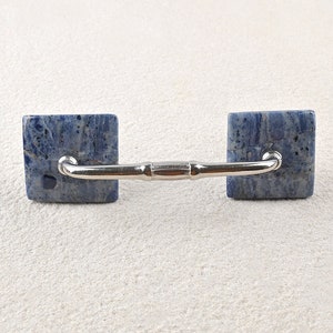 Może przedstawiać: Srebrny uchwyt do szafki z dwoma kwadratowymi gałkami z niebieskiego i białego marmuru.