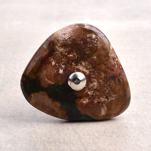 Könnte beinhalten: Ein brauner, weißer und grüner Achat-Stein mit einem silbernen Metallakzent. Der Stein hat eine unregelmäßige Form und ein natürliches, organisches Aussehen.