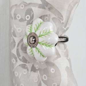 May include: White ceramic curtain tieback with a green floral design. The tieback has a silver metal ring.