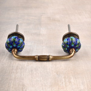 May include: A blue and green ceramic drawer pull with a brass handle. The pull has a floral design and is attached to a brass base.