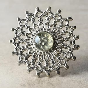 May include: A silver filigree knob with a clear glass centre. The knob is circular in shape and has a delicate, intricate design.