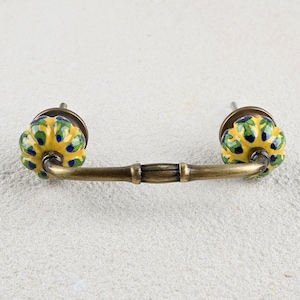 May include: A brass cabinet pull with yellow, green and blue ceramic knobs. The pull has a decorative, fluted design.