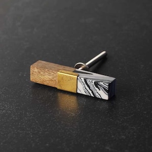 Puede incluir: Un pomo de armario rectangular con una parte superior de madera, un acento de metal dorado y una parte inferior de mármol blanco y negro.
