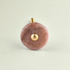 Può includere: Un pomello per armadio in marmo rosa e bianco con un accento in metallo dorato.