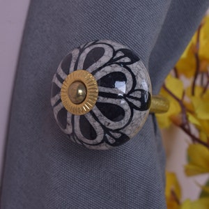 Könnte beinhalten: Ein schwarzer und weißer Keramik-Knopf mit goldener Mitte, befestigt an einer goldenen Metallstange. Der Knopf hat ein florales Design.