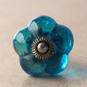 Puede incluir: Un pomo de armario de vidrio azul con un centro de metal plateado.