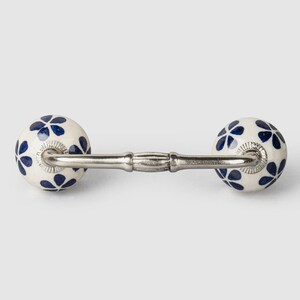 May include: A white ceramic drawer pull with a silver metal bar connecting two round knobs. The knobs are decorated with a blue floral pattern.
