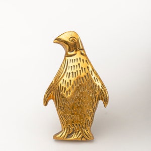 May include: A gold-colored penguin figurine with a detailed design. The penguin is standing upright with its wings outstretched.