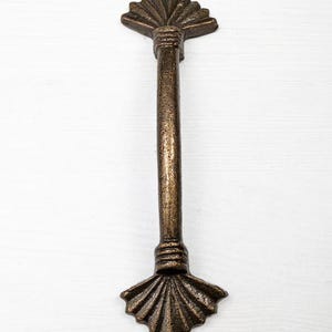 May include: A bronze cast iron drawer pull with a decorative fan-shaped design at each end.
