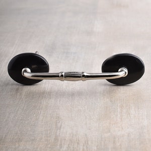 May include: A silver cabinet pull with black ceramic knobs. The pull has a simple, curved design.