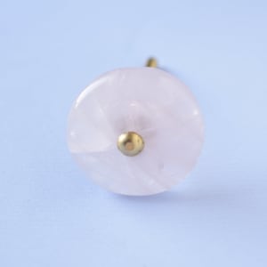 May include: A pink rose quartz knob with a gold metal base. The knob is round and has a smooth, polished surface.