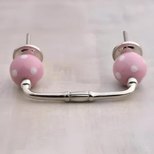 May include: A pink ceramic drawer pull with white polka dots and a silver metal bar.