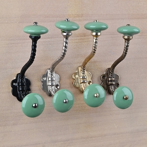 May include: Four decorative hooks with a twisted metal stem and a ceramic knob. The knobs are a light green color. The hooks are in black, silver, gold, and bronze.