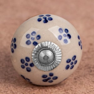 May include: A white ceramic knob with a blue floral pattern and a silver metal center. The knob is round and has a smooth surface.