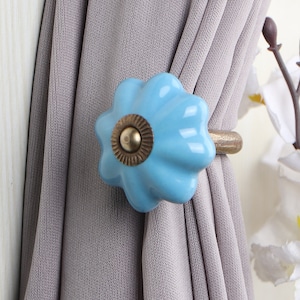 May include: A light blue ceramic curtain tieback with a gold metal ring. The tieback is shaped like a flower with a fluted design.