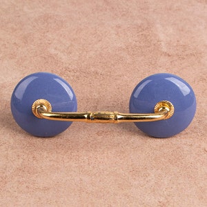 May include: A blue ceramic cabinet knob with a gold metal arm. The knob is round and has a smooth finish.