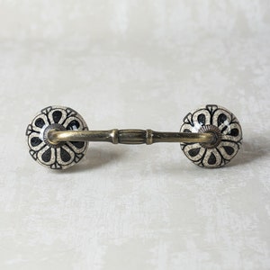 May include: A pair of black and white ceramic drawer pulls with a floral design. The pulls are attached to a brass bar.