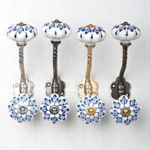Pode incluir: Quatro ganchos de cerâmica com um design floral azul e branco. Os ganchos são fixados a uma base de metal torcido e estão disponíveis em acabamentos prata, dourado e preto.