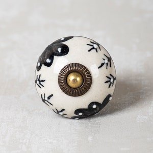 May include: White ceramic knob with a black floral design and a gold metal accent.