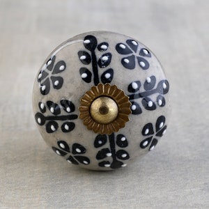 May include: A grey ceramic knob with a black and white floral design and a gold metal accent.