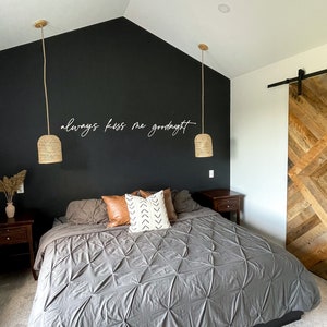 May include: A bedroom with a black accent wall featuring the text "always kiss me goodnight". The room has a large bed with a grey comforter and a wooden sliding barn door.
