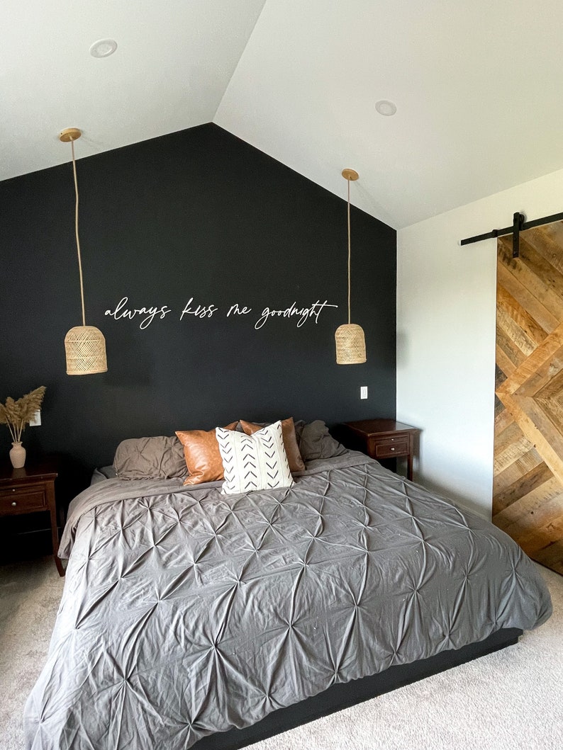 May include: A bedroom with a black accent wall featuring the text "always kiss me goodnight". The room has a large bed with a grey comforter and a wooden sliding barn door.