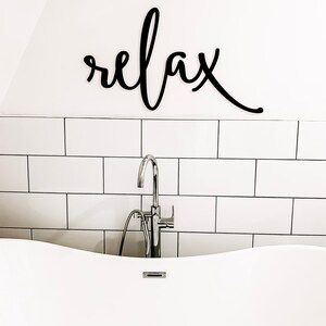 May include: A white bathtub with a chrome faucet and a black wooden sign that says "relax" above it.