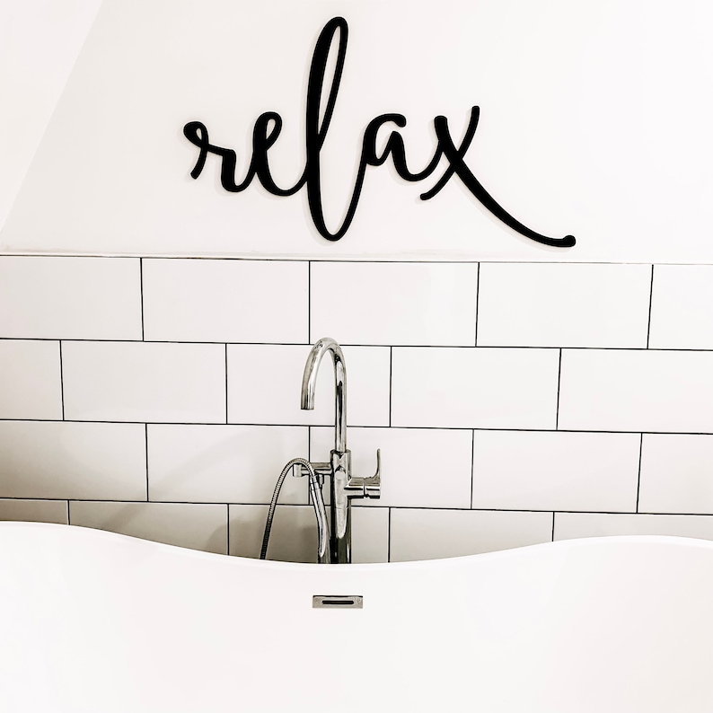 May include: A white bathtub with a chrome faucet and a black wooden sign that says "relax" above it.