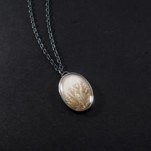May include: Oval pendant necklace with a silver chain. The pendant features a white background with a brown, tree-like pattern encased in a silver bezel. The necklace is displayed against a black background.