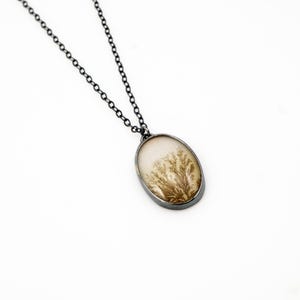 May include: Oval pendant necklace with a silver-tone chain. The pendant features a cream-colored stone with a brown, tree-like pattern. The pendant is framed in a silver-tone metal.