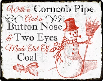 May include: A vintage-style metal sign with a red and white illustration of a snowman holding a broom and a corncob pipe. The text on the sign reads: "With a Corncob Pipe And a Button Nose & Two Eyes Made Out Of Coal."