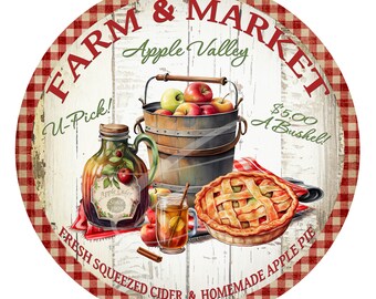 Può includere: Un cartello rotondo con un bordo a scacchi rosso e bianco. Il cartello dice "Farm & Market Apple Valley" in bianco con un "U-Pick!" e un "€ 5,00 Il Bushel!" in verde. Il cartello dice anche "Succo di mele fresco spremuto & torta di mele fatta in casa". Il cartello ha uno sfondo in legno bianco rustico e presenta un secchio di mele, un barattolo di sidro di mele e una torta.