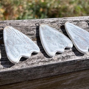 May include: Five white and grey triangular pendants with a textured, weathered finish. Each piece features a rounded top with a small metal loop for hanging and a three-pronged bottom edge, resembling a stylized animal paw or footprint.