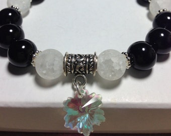 May include: Black and white beaded bracelet with a silver charm in the shape of a snowflake. The bracelet has a silver spacer bead with an ornate design.