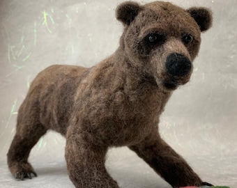 May include: A brown bear with a red and green fish in its paw. The bear is standing on a light gray surface.