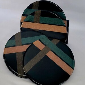 Puede incluir: Conjunto de cuatro posavasos redondos con un patrón geométrico. Los posavasos son negros con rayas marrones y verdes.