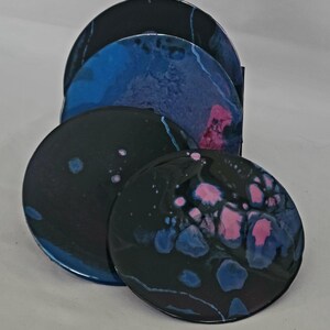 Puede incluir: Conjunto de cuatro posavasos redondos con diseños abstractos en negro, azul y rosa. Los posavasos tienen un acabado brillante.