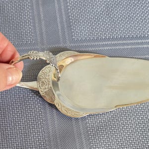 以下が含まれることがあります： 銀色の金属製ケーキサーバー。細長く滑らかで平らな刃と、花や葉の複雑な彫刻が施された装飾的なハンドルが特徴です。ハンドルは上向きにカーブしており、ケーキやデザートを取り分ける際に握りやすい形状になっています。