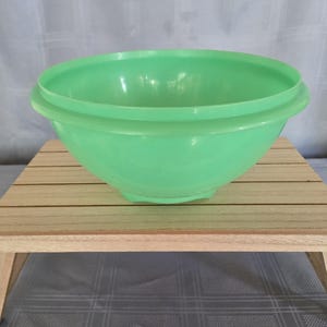 May include: A light green mixing bowl with a smooth, matte finish and a wide, rounded rim. The bowl features a deep, circular basin with a slightly tapered base, constructed from a solid, opaque material with a consistent pastel green colour.