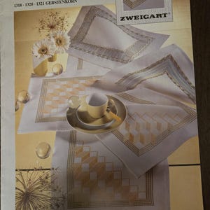 May include: A magazine cover with needlework ideas, including the text "STICK-IDEE" and "ZWEIGART". The image displays embroidered placemats and a cup and saucer set. The placemats feature geometric patterns in yellow and brown hues.