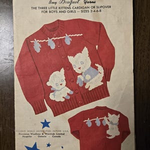 May include: Vintage knitting pattern cover featuring a red cardigan with white and blue kitten designs. The text reads "KNIT O GRAF" and "THE THREE LITTLE KITTENS CARDIGAN OR SLIPOVER FOR BOYS AND GIRLS - SIZES 2-4-6-8". The cover is slightly worn.