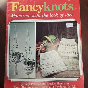 Puede incluir: Una portada de libro vintage roja titulada "Fancyknots", que presenta proyectos de macramé. La portada muestra colgadores de plantas y bolsos, con el texto "Macramé con aspecto de encaje". El libro incluye proyectos de Judy Peacher y Lucille Hammons.