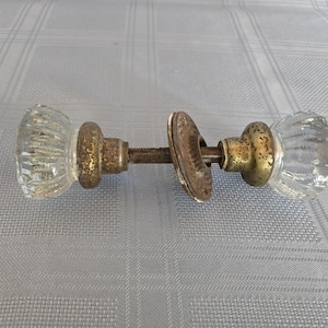 Könnte beinhalten: Antikes Türknauf-Set aus Glas mit klarem, geripptem Glasdesign. Die Metallkomponenten haben ein angelaufenes, gealtertes Aussehen. Das Set enthält zwei Knöpfe, eine Verbindungsstange und eine Montageplatte.