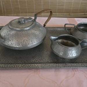 以下が含まれることがあります： 銀製のティーセット。ティーポット、クリーマー、シュガーボウルが銀のトレイに乗っています。セットはハンマード仕上げです。