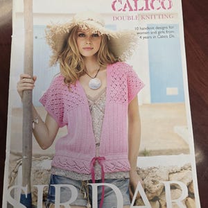 Op de afbeelding: Een tijdschriftomslag met een vrouw in een roze gebreid vest en een strohoed. De tekst luidt "CALICO DOUBLE KNITTING" en "10 handgebreide ontwerpen voor vrouwen en meisjes vanaf 4 jaar in Calico Dk". De cover heeft een lichte, zomerse uitstraling.