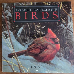 Peut inclure: Couverture de livre carrée avec une peinture d'un cardinal rouge perché sur une branche enneigée. Le titre "ROBERT BATEMAN'S BIRDS" est affiché dans un encadré noir avec des lettres rouges, et l'année "1996" est en bas.